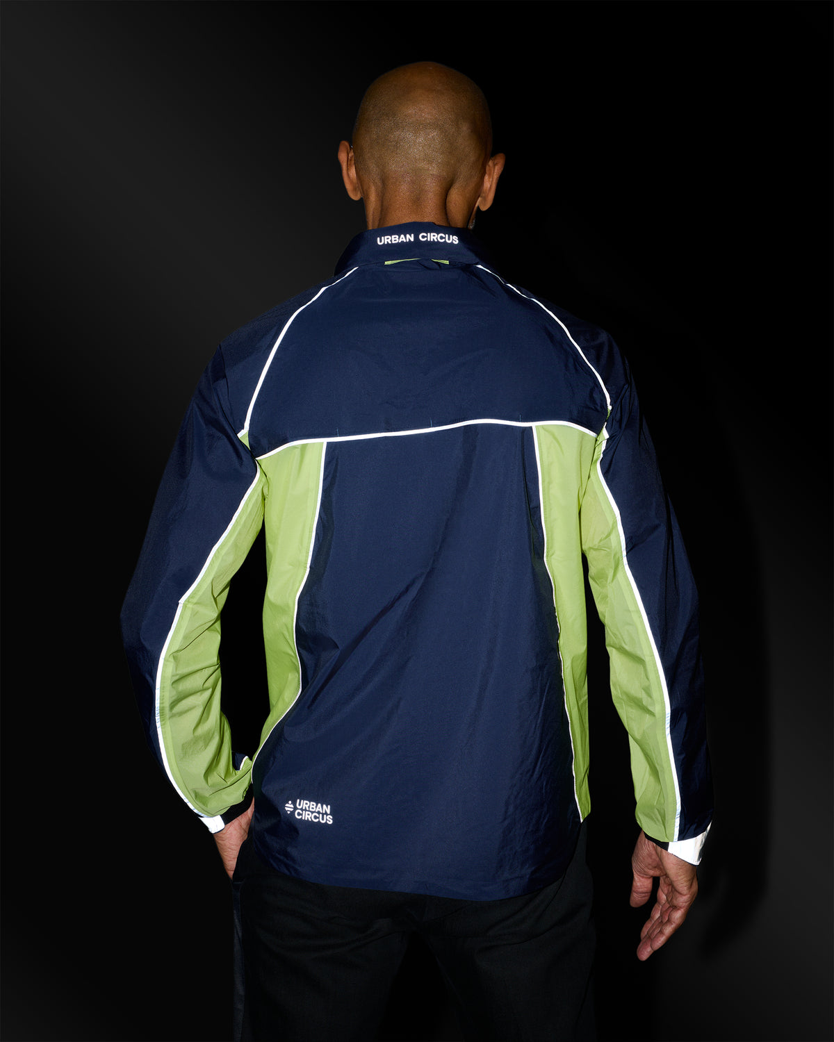veste ultra légère de sport outdoor jaune bleue marine avec détails réfléchissants de dos sur homme la nuit