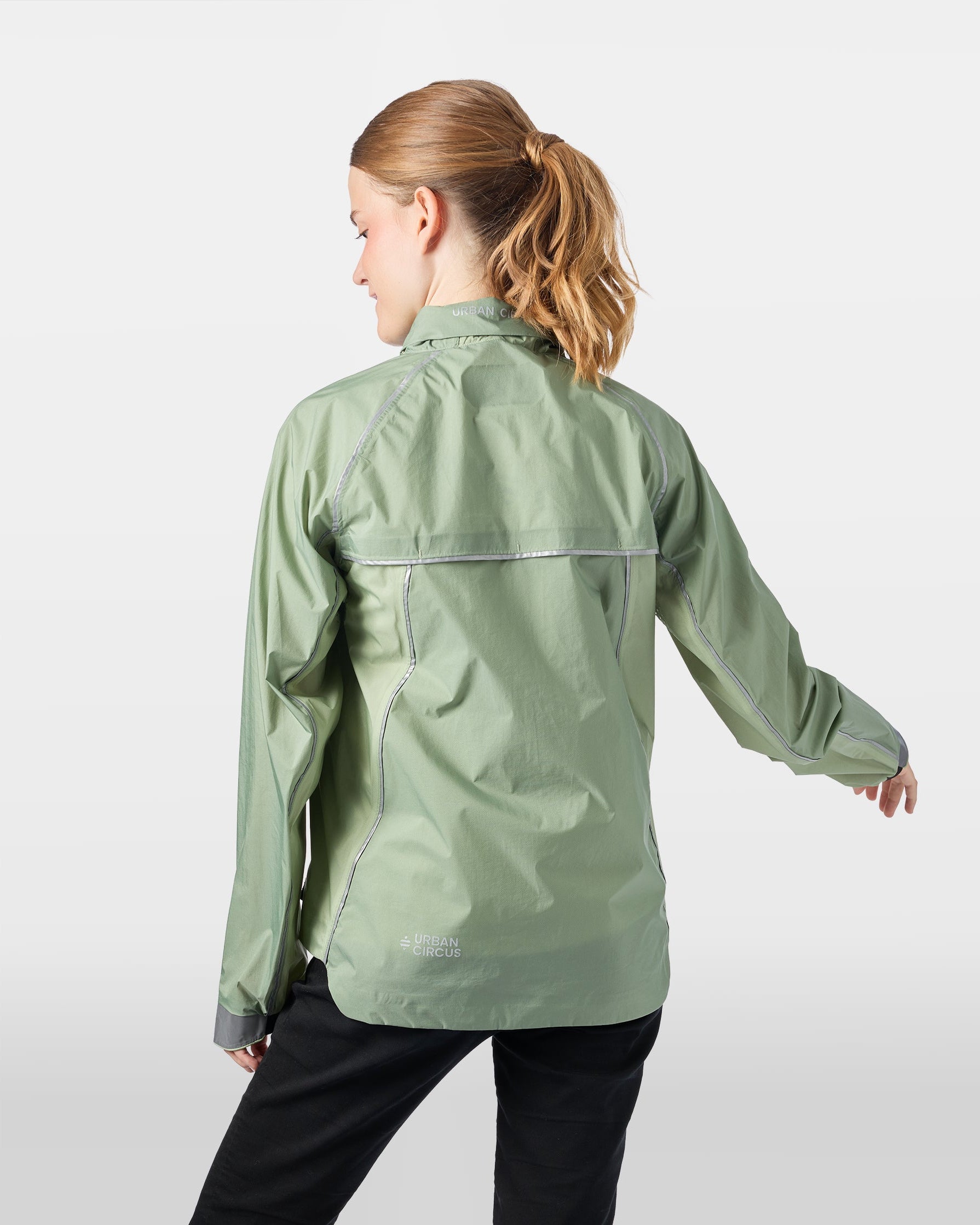 Ultralicht en ademend jack voor outdooractiviteiten in saliegroen, gedragen door een vrouw van achteren, met de capuchon opgeborgen in de kraag